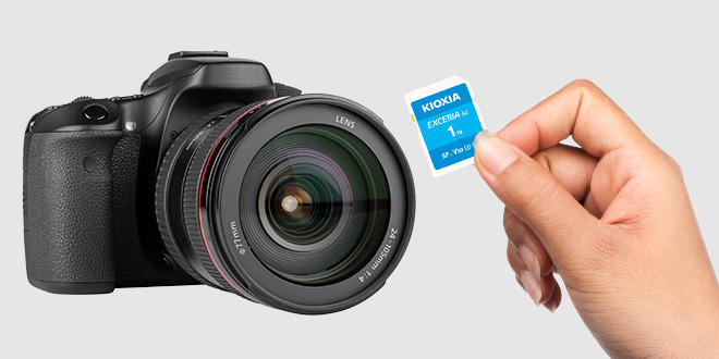Χέρι που κρατάει μια κάρτα SD EXCERIA G2 μπροστά από μια φωτογραφική μηχανή DSLR